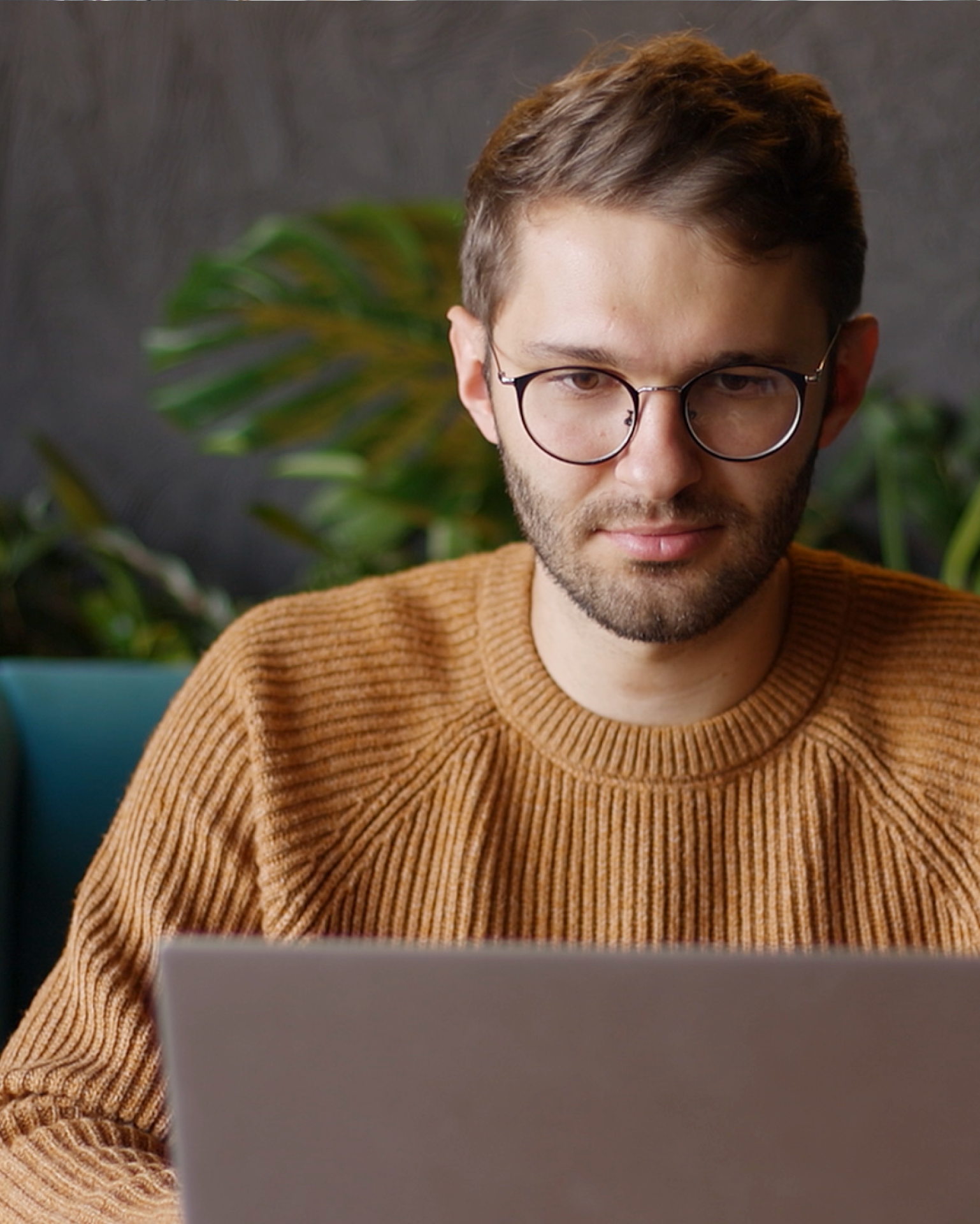 Ein Mann mit Brille in einem braunen Pulli, der vor einem Computer oder Laptop sitzt.