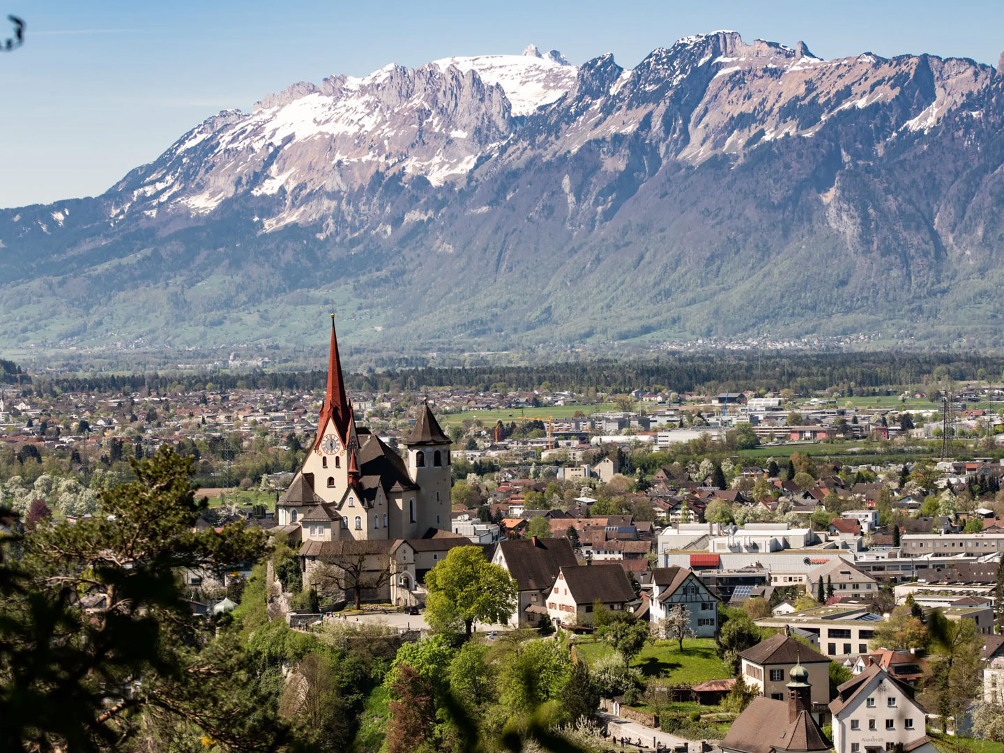 In Rankweil befindet sich der Vorarlberger Standort von Allgeier inovar, erkannbar an der Kirche im Vordergrund und dem Alpenmassiv hinter dem Rheintal im Hintergrund.