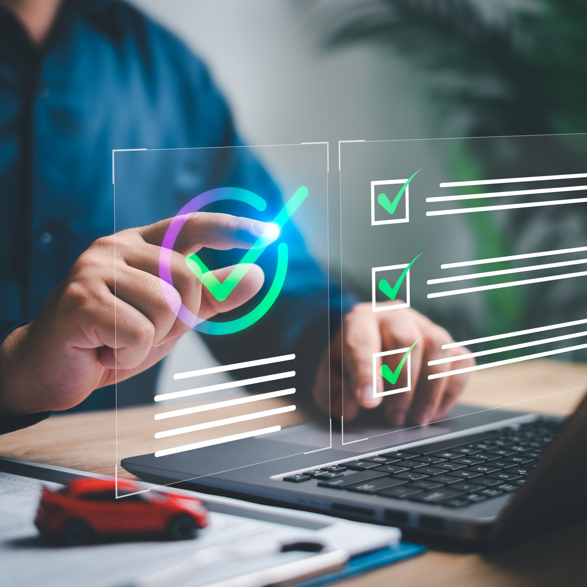 Mann in blauem Hemd am Schreibtisch mit Laptop und rotem Spielzeugauto der per Touch eine virtuelle Funktion einer Lösung von Allgeier inovar bedient.