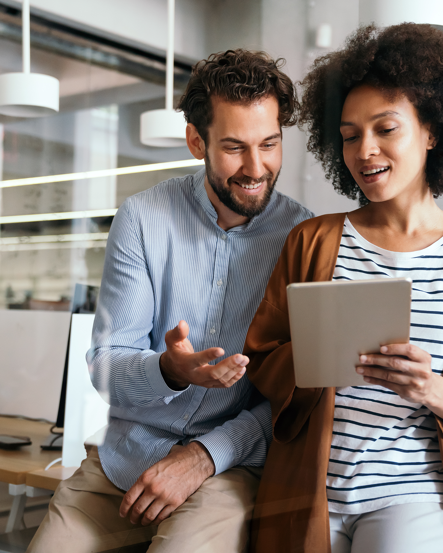 Mann und Frau sitzen auf Tisch und betrachten auf Tablet, wie Projektmanagement mit Software von Allgeier inovar optimal gesteuert wird.