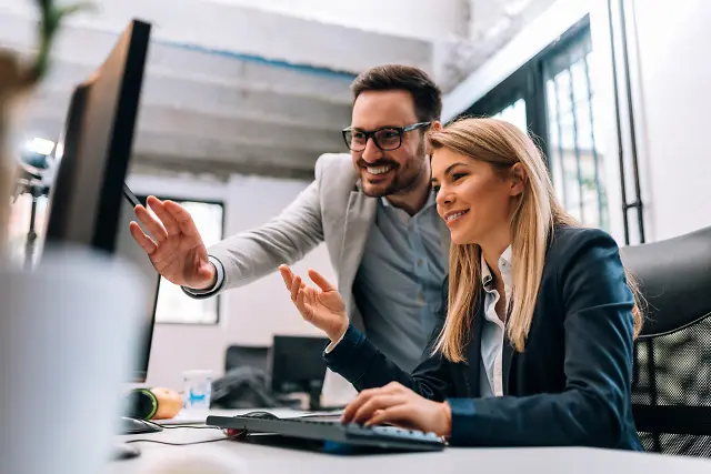 Frau und Mann mit Brille und Business Outfit arbeiten am Schreibtisch und betrachten am Monitor das KundenPortal von Allgeier inovar für moderne Kundenkommunikation.