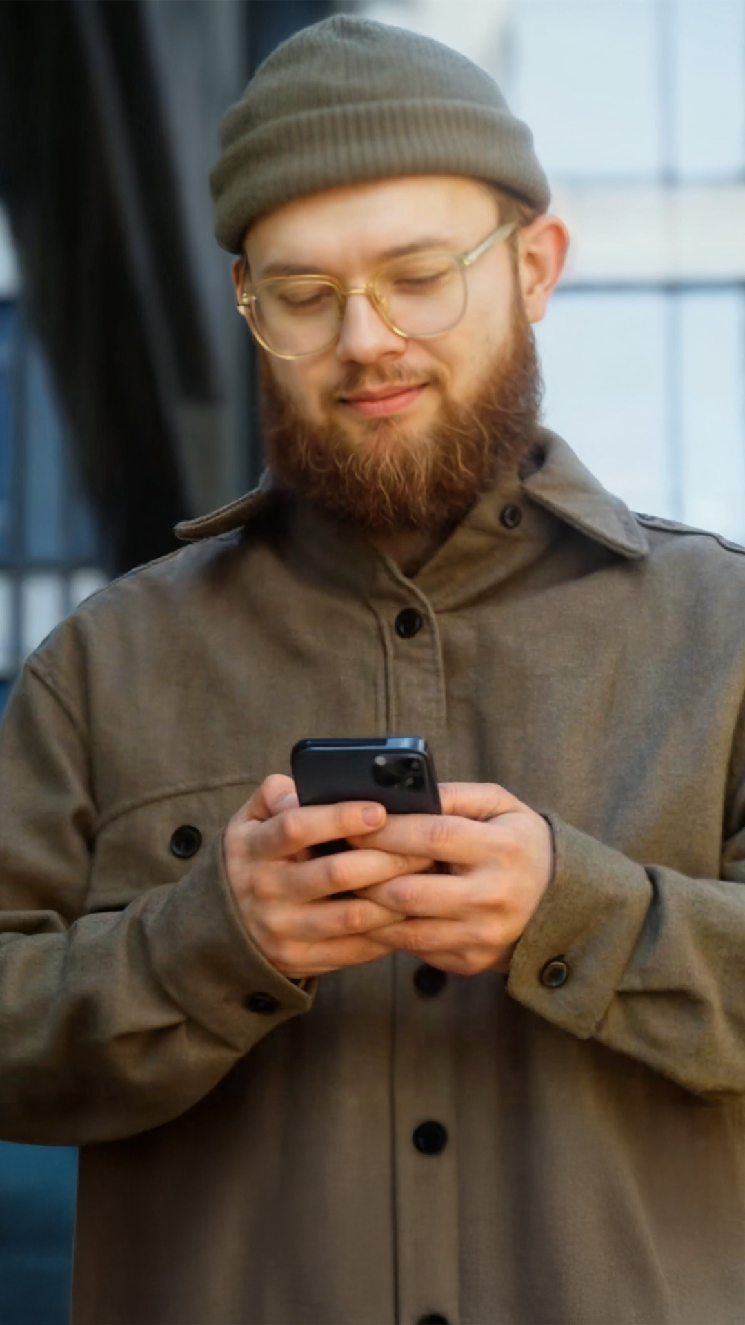 Junger Mann mit Bart, Brille und Mütze nutzt auf dem Handy das KundenPortal von Allgeier inovar.