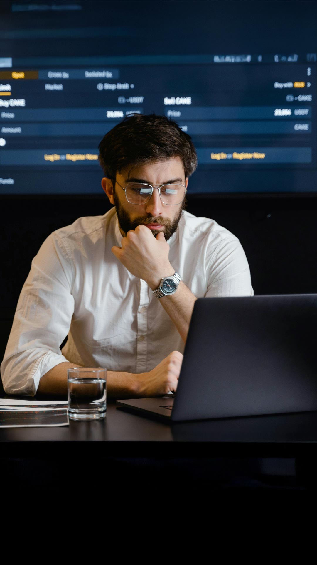 Mann mit dunklem Haarschopf, Bart und Brille sitzt am Tisch und schaut in einen Laptop mit Software von Allgeier inovar. Daneben ein Glas Wasser, im Hintergrund ein Datenmonitor.