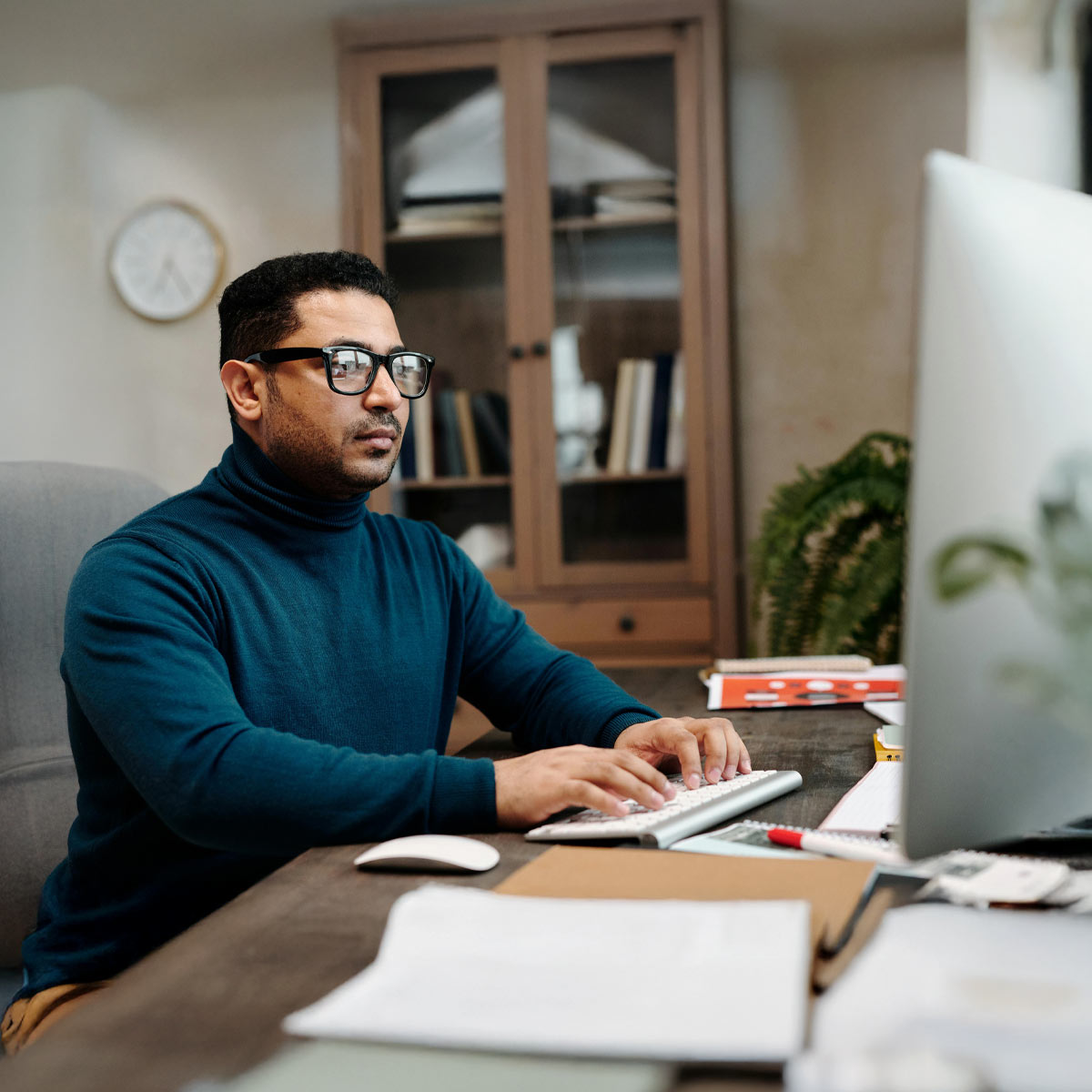 Mann mit schwarzer Brille sitzt an Schreibtisch im Homeoffice und beschäftigt sich mit Lösung für E-Rechnungen für syntona® logic von Allgeier inovar.