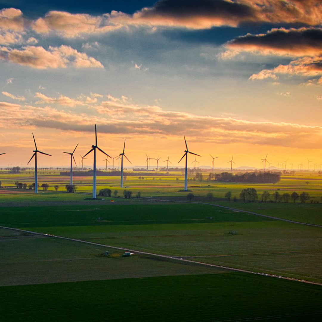 Die Silhouette von Windkrafträdern vor gelb-wolkigem Himmel mit AURELO Energiepark Manager für die kaufmännische Betriebsführung von Allgeier inovar.