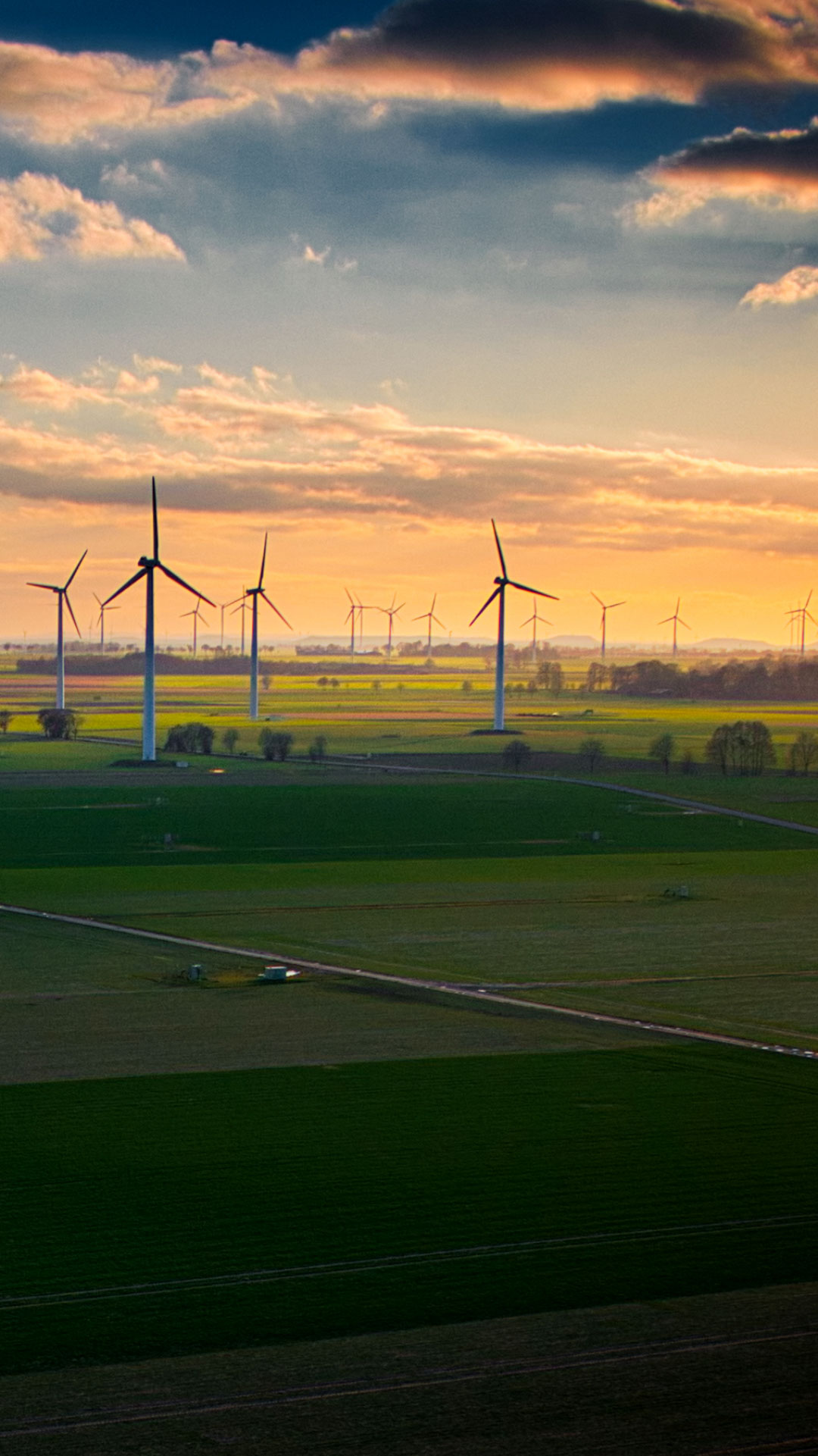 Die Silhouette von Windkrafträdern vor gelb-wolkigem Himmel mit AURELO Energiepark Manager für die kaufmännische Betriebsführung von Allgeier inovar.