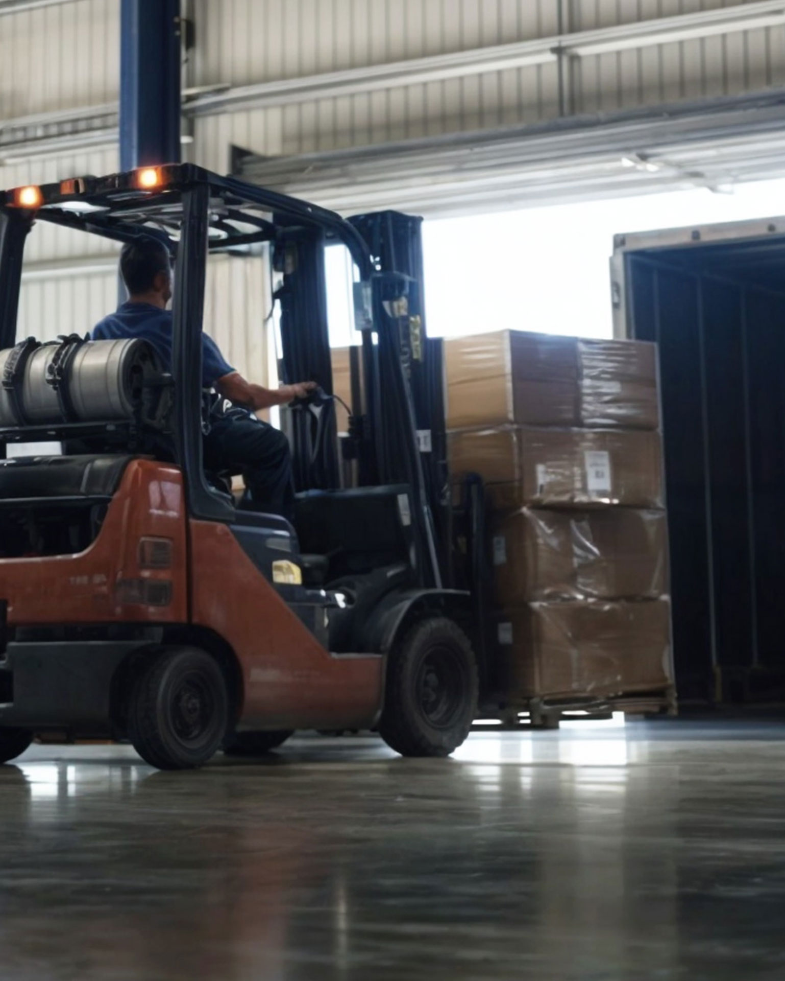 Roter Gabelstapler in Warenlager mit Paketen auf Paletten wird von Mann gesteuert, mit der Lösung für Warehouse Management von Allgeier inovar.