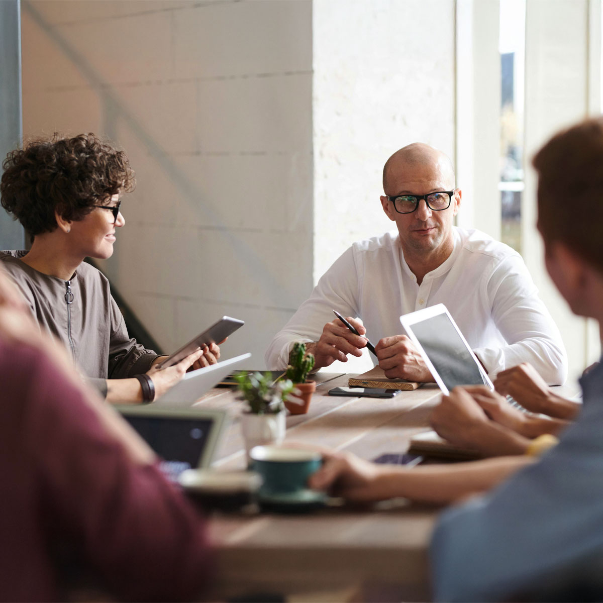 Vier Menschen am Tisch mit verschiedenen Devices in der Hand diskutieren Personalprozesse mit der Software von Allgeier inovar. Am deutlichsten frontal ein Mann mit Brille und weißem Hemd.