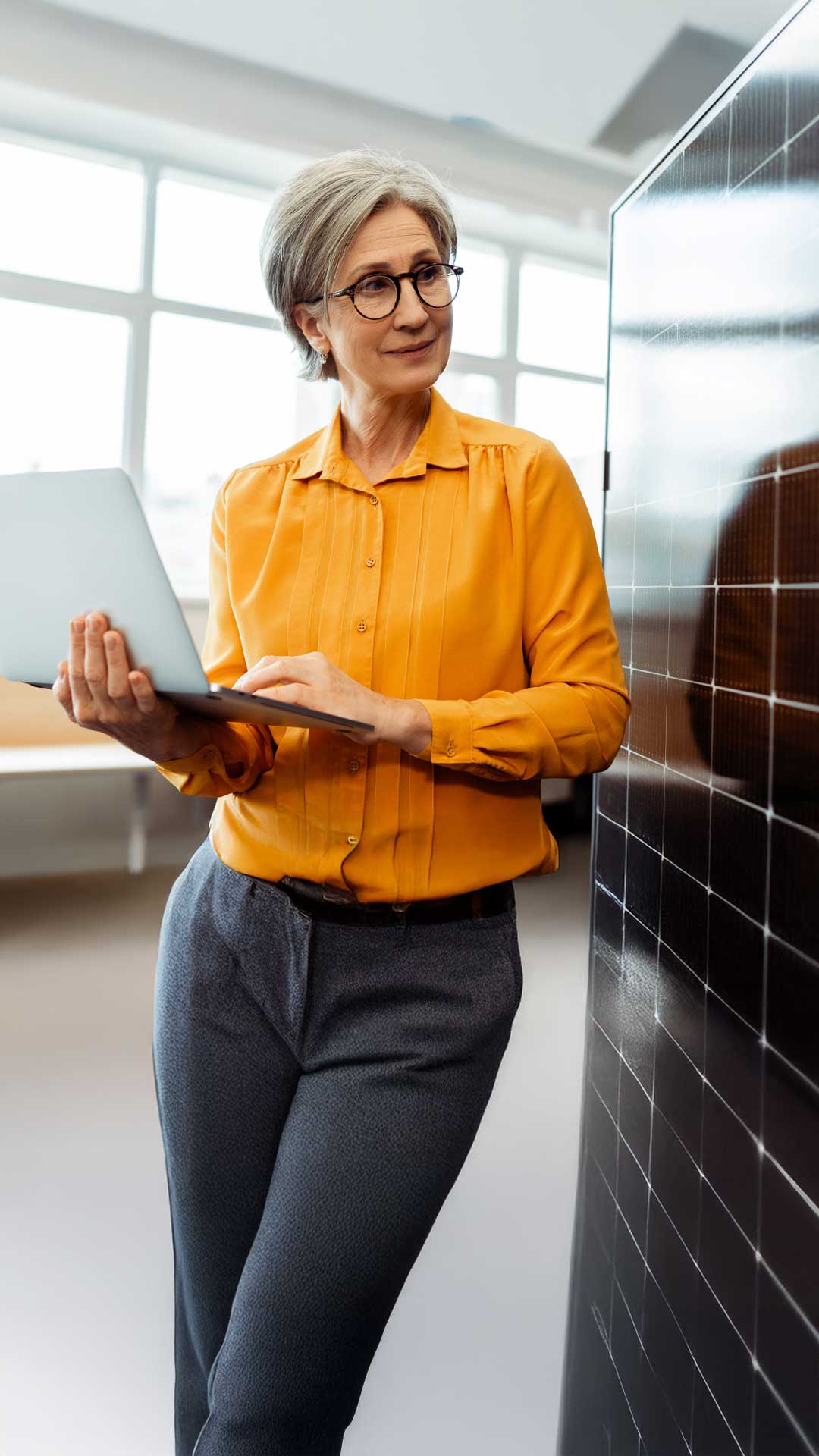 Frau mit oranger Bluse und runter Brille trägt Laptop und schaut zur Seite, um das Rechnungsmanagement für Erneuerbare Energie zu erledigen.