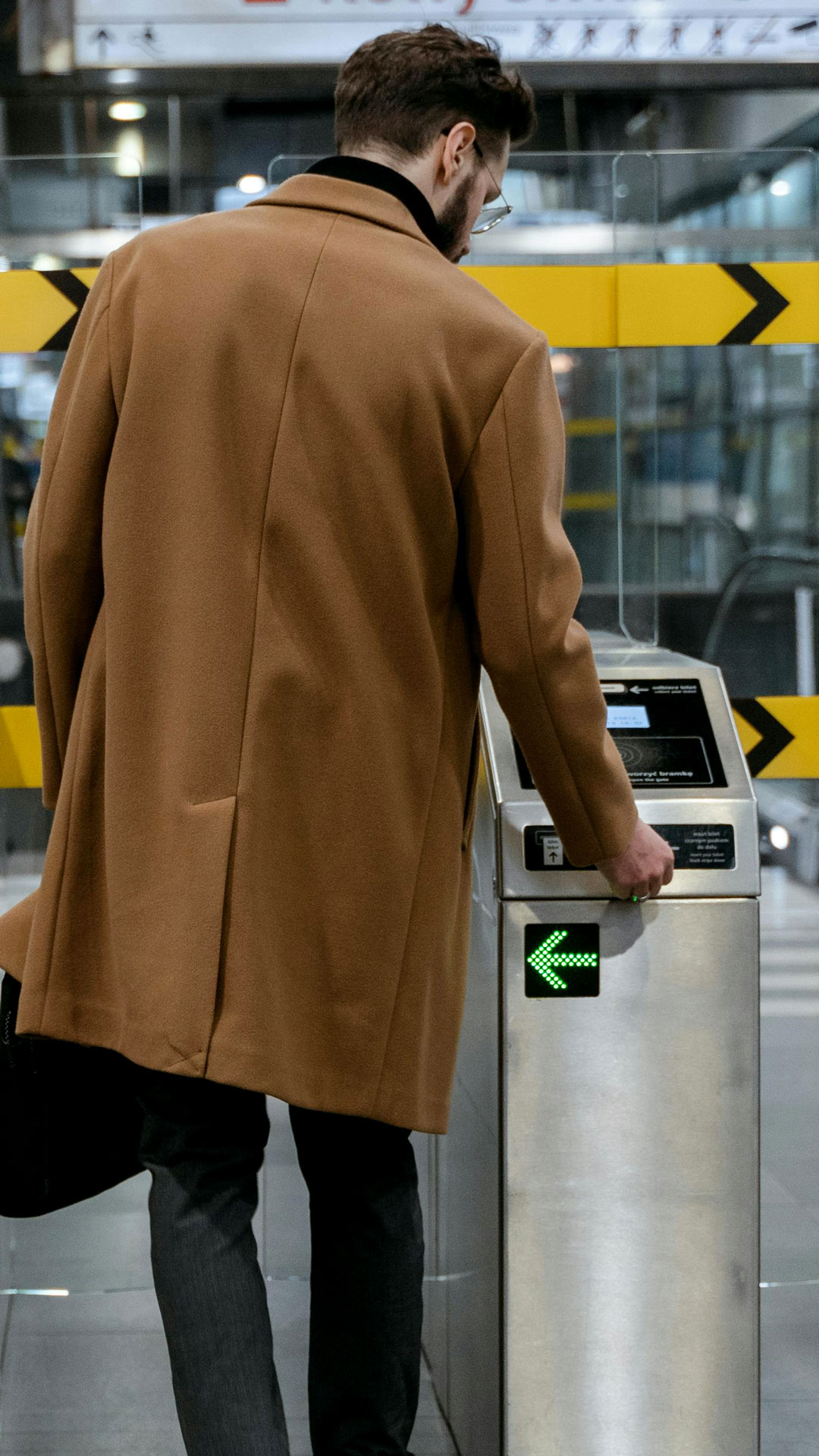 Mann mit braunem Mantel und Aktentasche steckt Ticket in Einlass-Automat mit dem Ticketsystem von Allgeier inovar.l