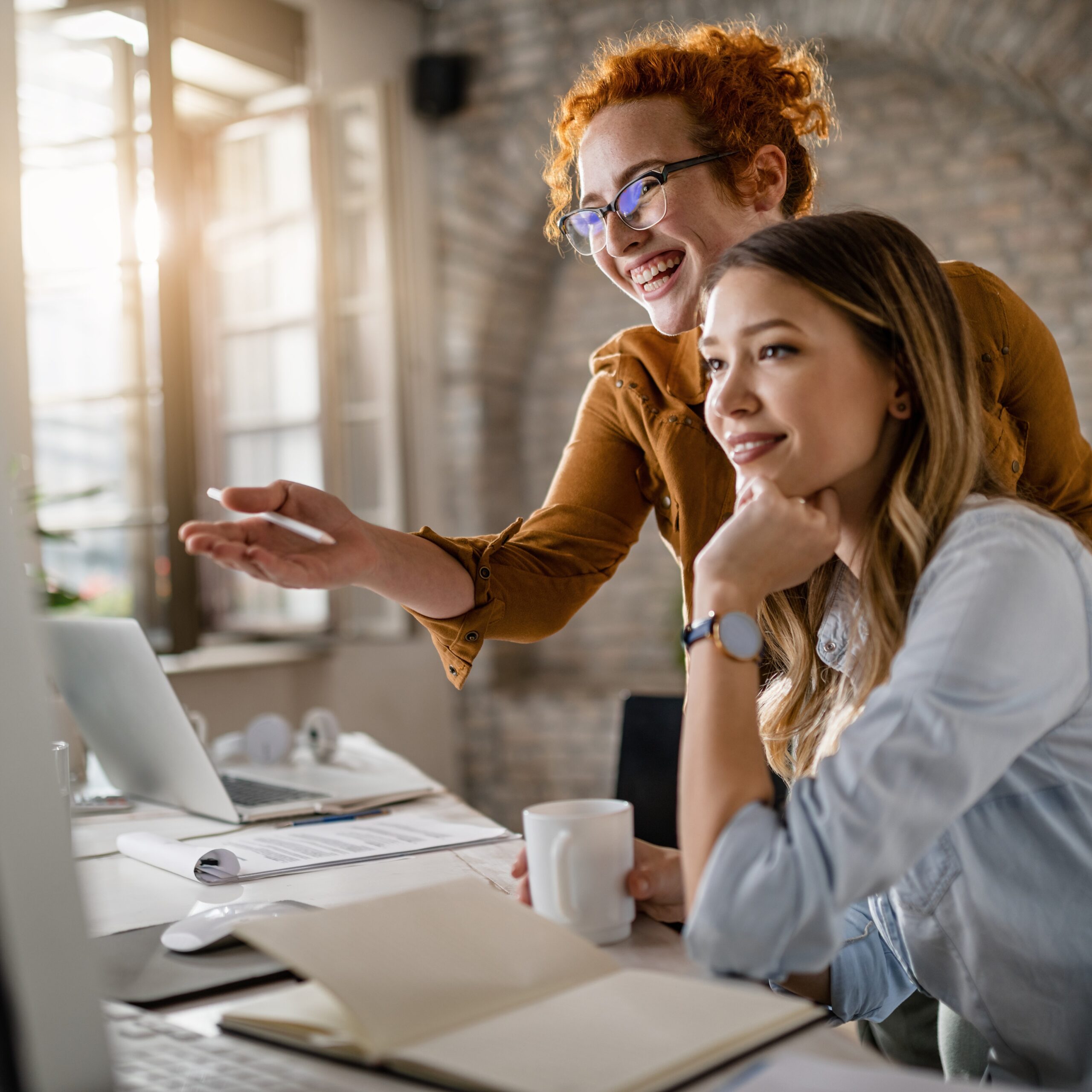 Zwei Frauen stehen vor einem Computer und schauen auf den Bildschirm sprechend.
