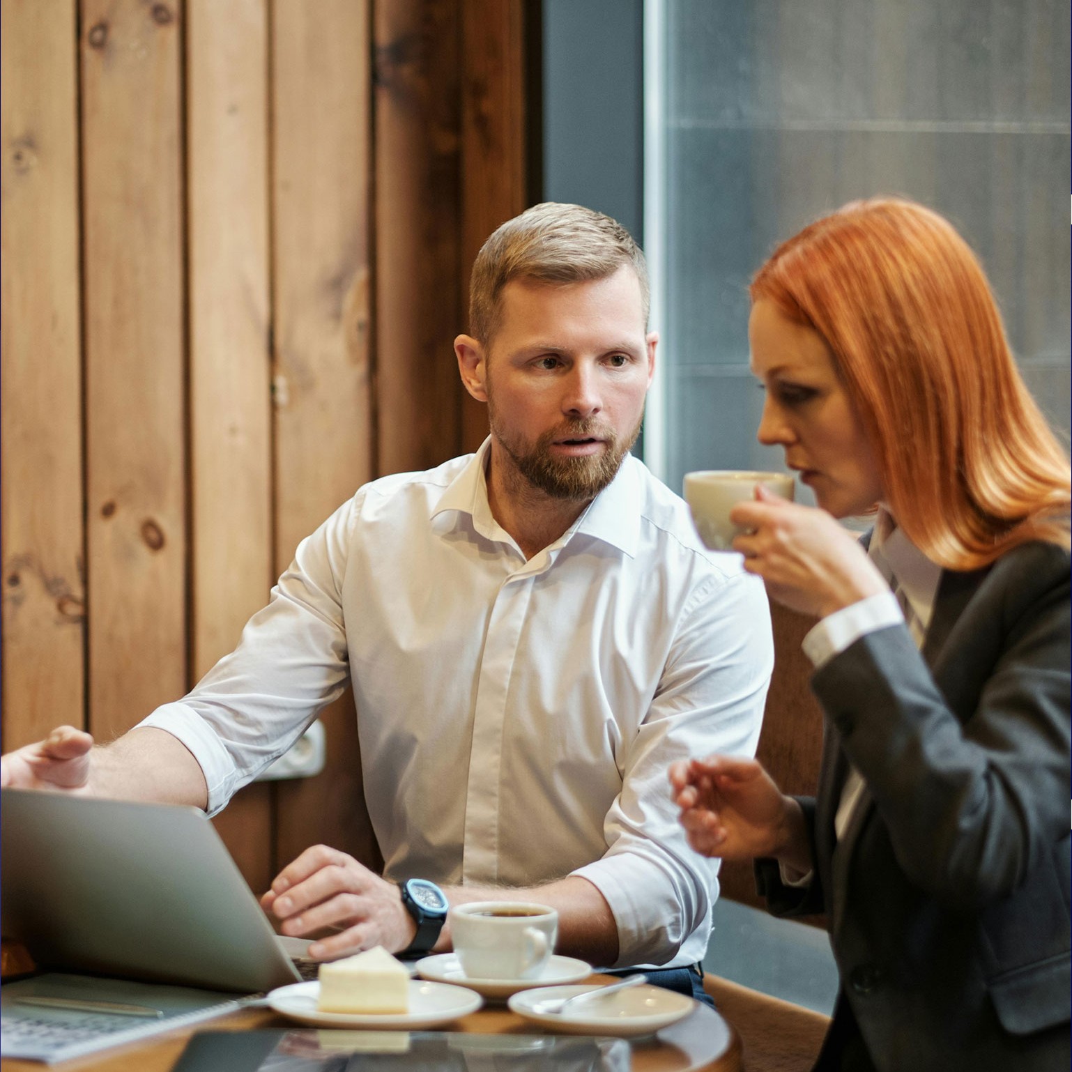 Mann erklärt Frau etwas auf dem Laptop während sie Kaffee trinken