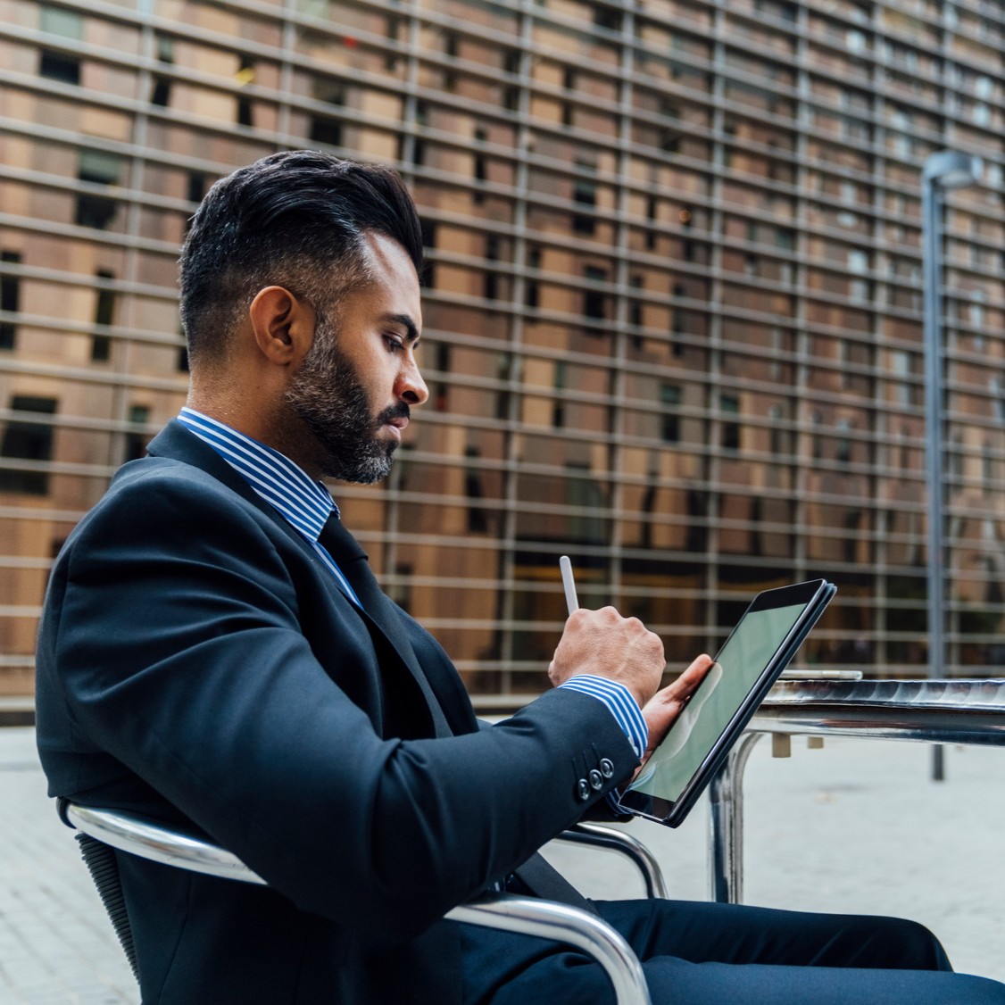 Ein Mann sitzt in einem Bürogebäude, trägt einen Anzug und hält ein Tablet in der Hand.