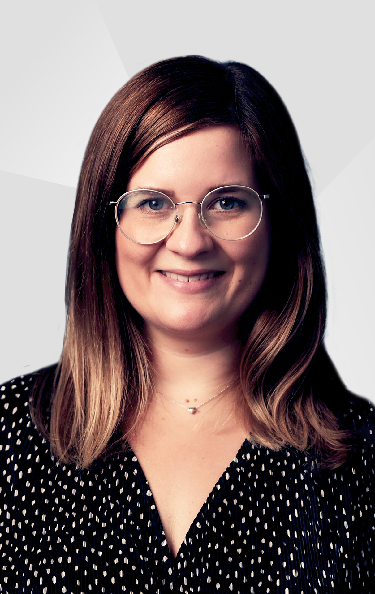Janine Freudenthal, Personalreferentin bei Allgeier inovar, schwarzes gepunktetes Oberteil vor einem grauen Hintergrund.