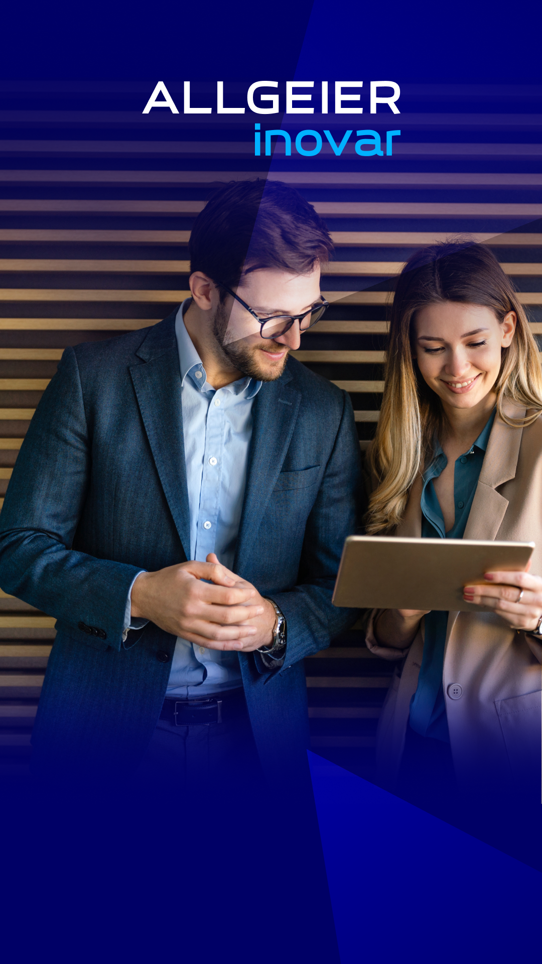 Ein Mann und eine Frau tragen Business Kleidung und schauen gemeinsam auf ein Tablet, das sie in der Hand hält. Sie stehen vor einer Bürowand mit Holzpanelen.